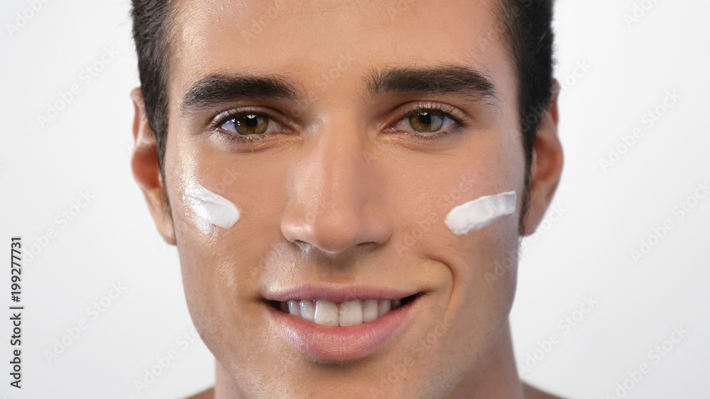 Obraz premium Close up of a man with moisturizer for his face smiling because he hydrates his skin and protects against impurities with anti-aging effects. Concept of: beauty and body care, creams, skincare