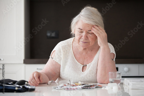  A gray-haired woman holds her head while sitting at a table.