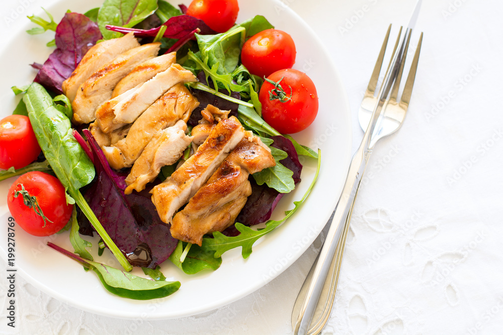 Sliced grilled chicken with green leaves salad on white plate