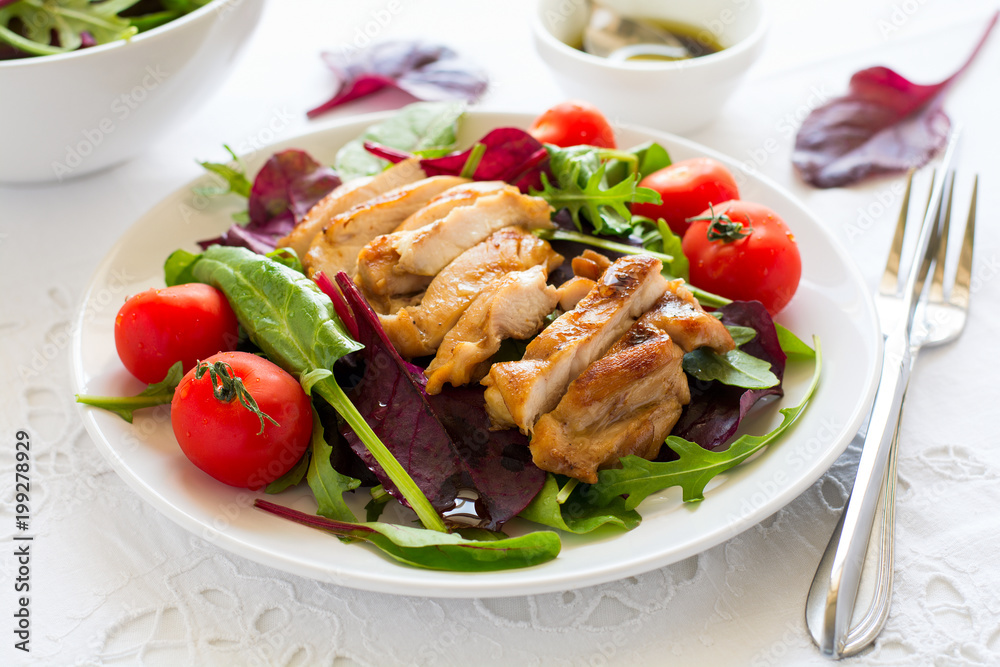 Sliced grilled chicken with green leaves salad on white plate