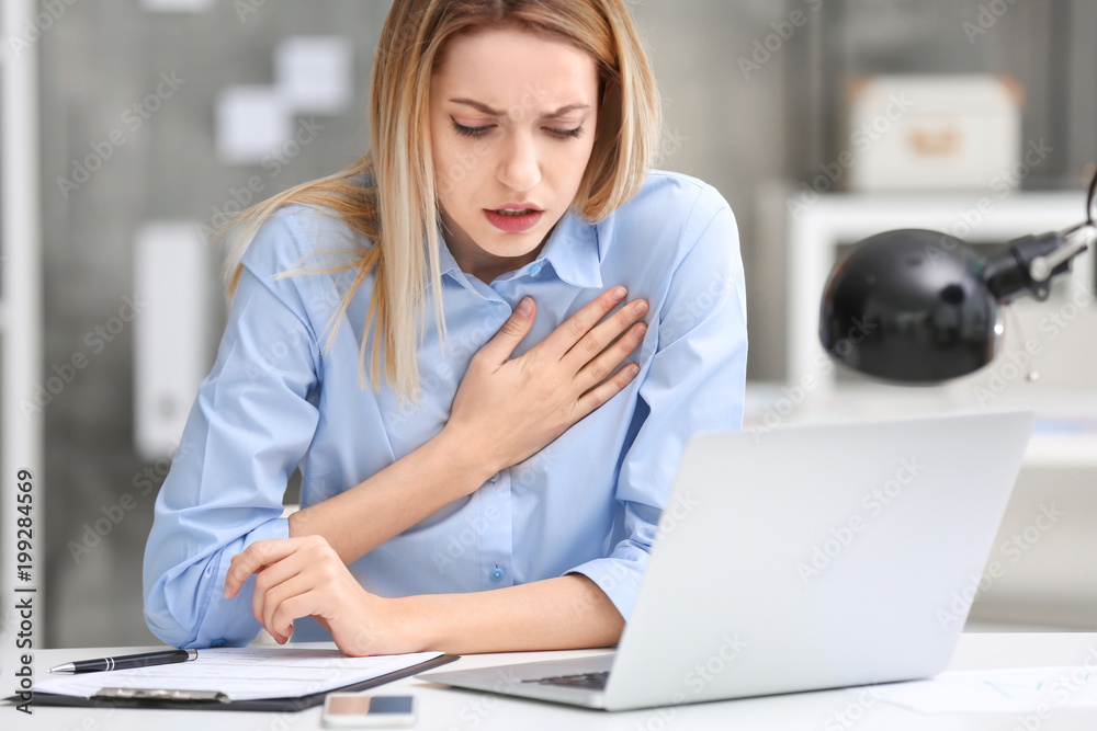Young woman suffering from chest pain in office Young woman suffering from chest pain in office