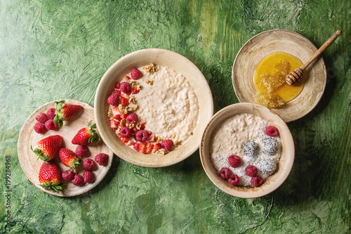 Sweet rice porridge pudding in ceramic plate with berries strawberry and raspberry, walnuts, honey over green texture background. Top view, space. photo