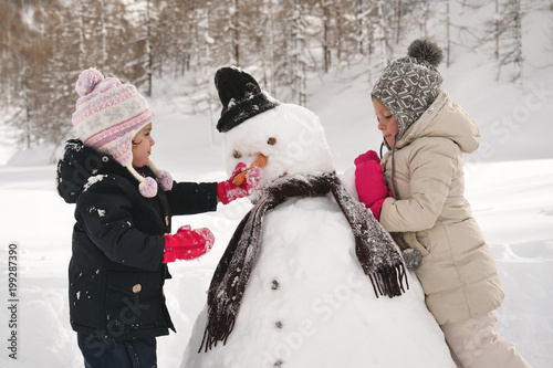 On a winter day, on the mountains with snow, a family plays with a snowman. Concept of: winter holidays, family, christmas, mountain