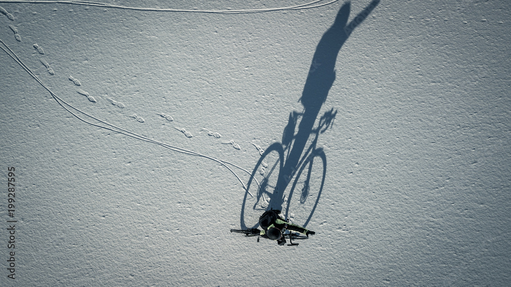 Conceptual image of bicyclist standing near by bike on the lake covered with ice and snow isolated on white, top view from drone. Huge shadow is seen on the snow.