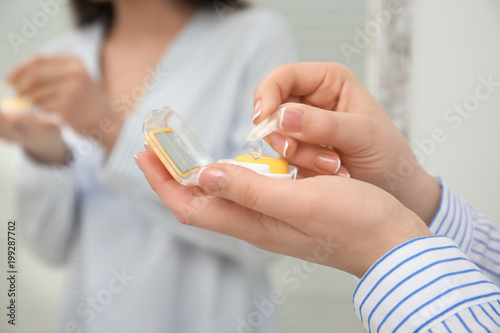 Young woman taking contact lens from container indoors
