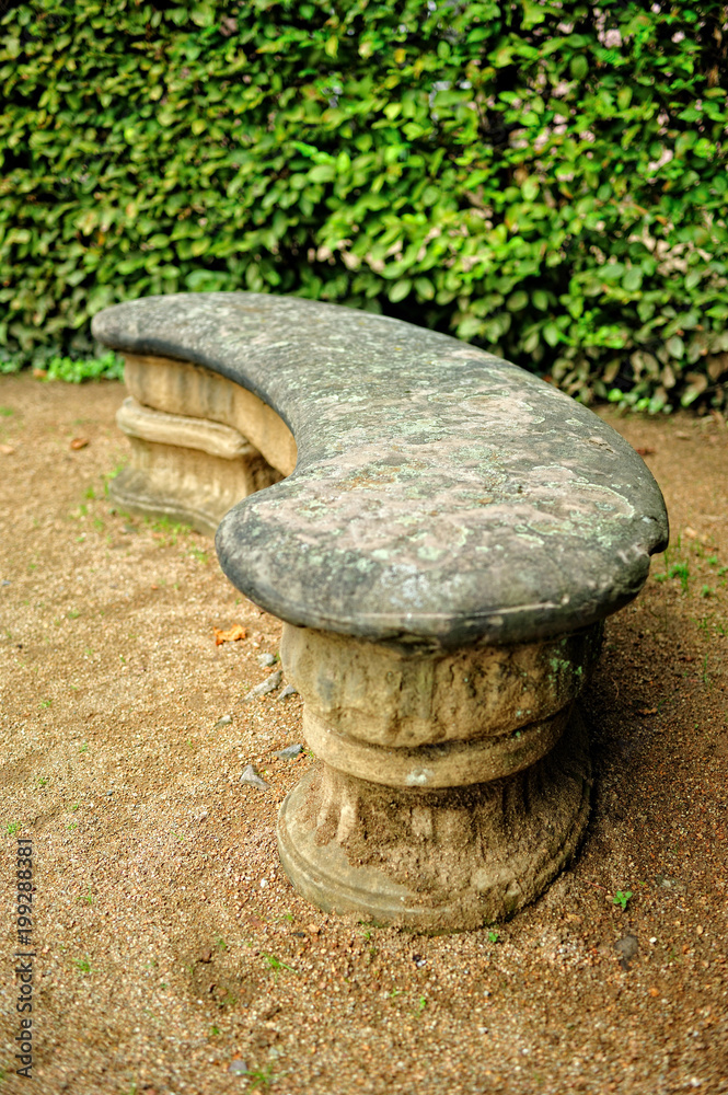 Obraz premium Old stone bench. Peaceful scene of a stone bench in the park surrounded by lush green vegetation.