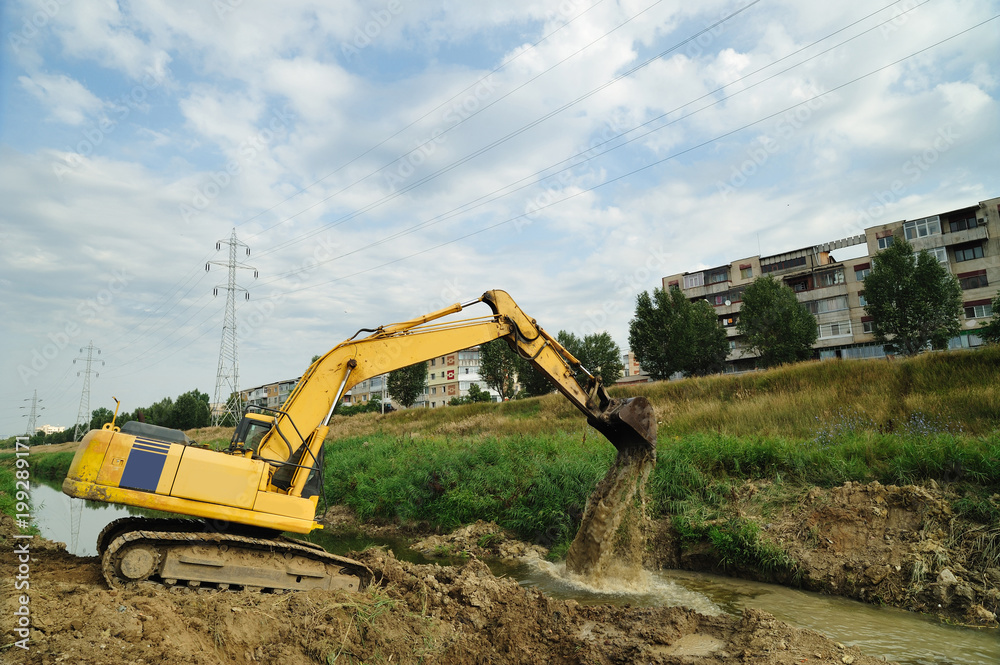 Crawler excavator at work. Forward activity of a crawler excavator who working on the riverbed site in town district. Crawler excavator at work. Forward activity of a crawler excavator who working on the riverbed site in town district.