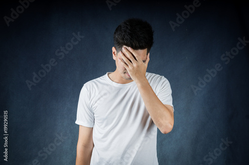 Terrible headache portrait handsome young asian man wearing a white t-shirt isolated on black background. Businessman concept. Asia people.