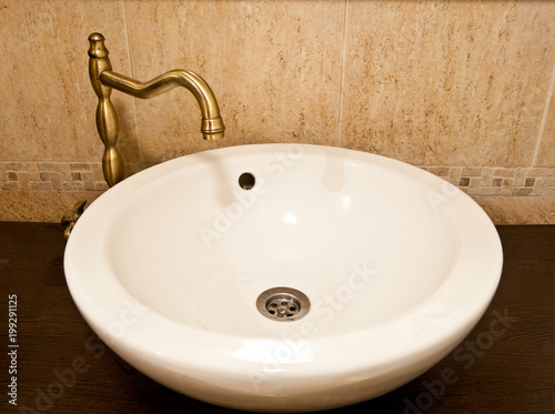 Ceramic sink inside bathroom. Rounded white ceramic sink with golden accessories inside bathroom. 
