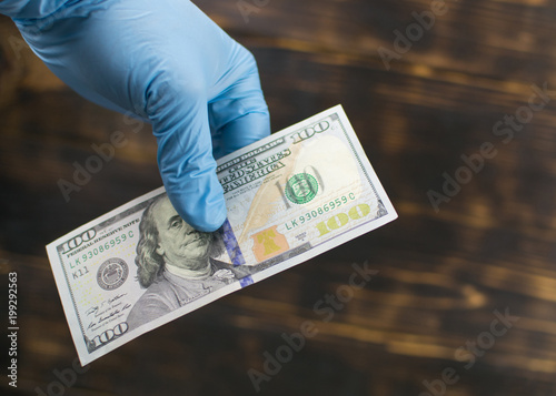 A gloved hand holds dollars. Dirty money.