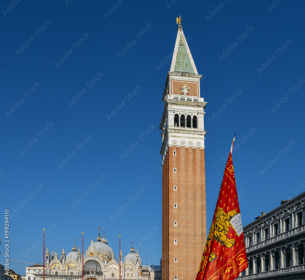 Winged Lion of St. Mark, the Venetian flag at San Marco square in Venice with the San Marco Campanile Tower.