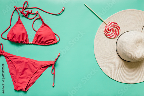 Red, pink bikini suit, lollipop, white hat on plain light cyan background. Empty space for copy, text, lettering. Summer vacation concept. Poster, banner, postcard template.