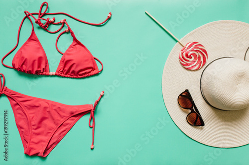 Red, pink bikini suit, lollipop, sunglasses, white hat on plain light cyan background. Empty space for copy, text, lettering. Summer vacation concept. Poster, banner, postcard template.