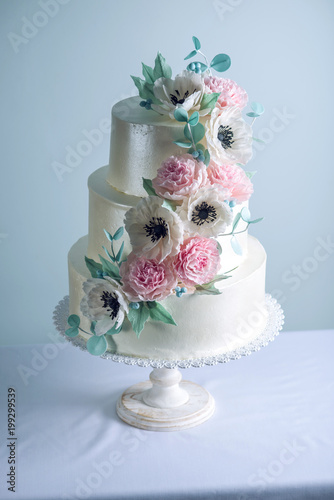 Beautiful three tiered white wedding cake decorated with flowers sugar pink peonies. Concept of elegant holiday desserts