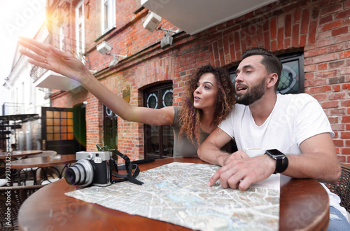 Young tourists drinking coffee at cafe and reading city map