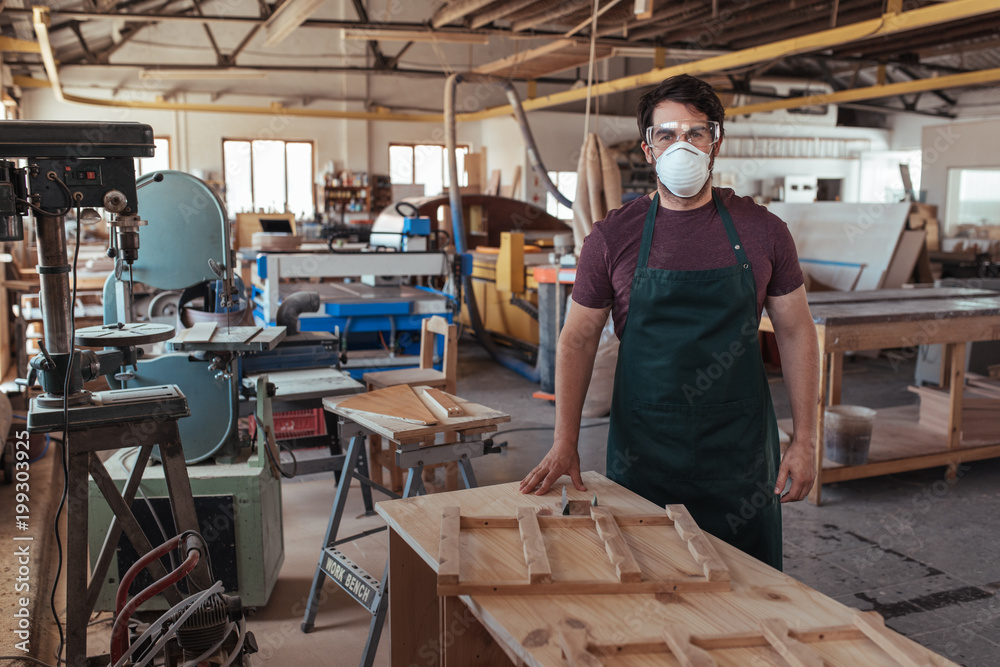 Young woodworker in protective workwear standing in his studio
