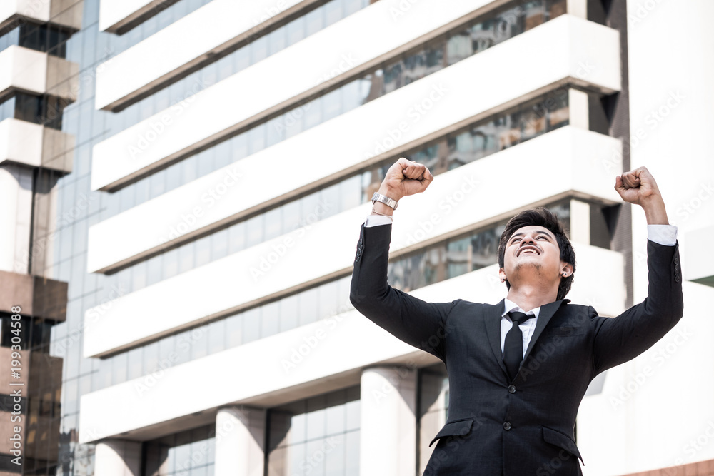 Portrait of young Asian businessman in black suit standing with office building background. Free space for text Portrait of young Asian businessman in black suit standing with office building background. Free space for text