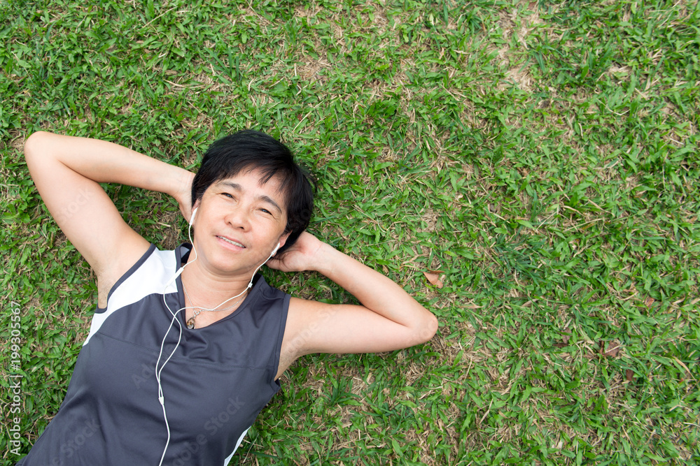 Summer close up portrait of senior Asian woman, laying on the grass listening to music Summer close up portrait of senior Asian woman, laying on the grass listening to music