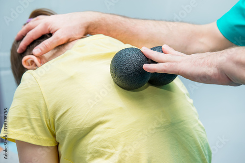 Woman at the physiotherapy receiving ball massage from therapist. A chiropractor treats patient's thoracic spine in medical office. Neurology, Osteopathy, chiropractic. Selective focus, Close up. photo