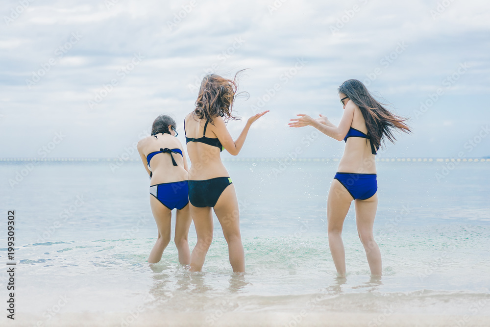 Naklejka premium Three pretty beautiful asian women wearing colourful swimwear bikini with hat having fun and relax sunbathing on the beach in the summer