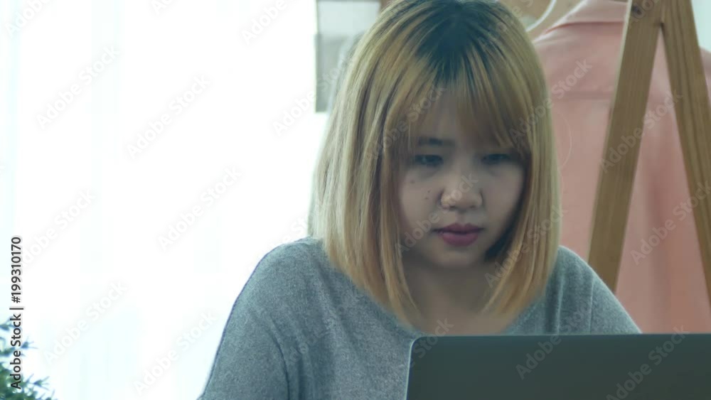 Beautiful young smiling Asian woman working on laptop while at home in office work space. Businesswoman working from home via portable computer writing on keyboard. Enjoying time at home. Beautiful young smiling Asian woman working on laptop while at home in office work space. Businesswoman working from home via portable computer writing on keyboard. Enjoying time at home.