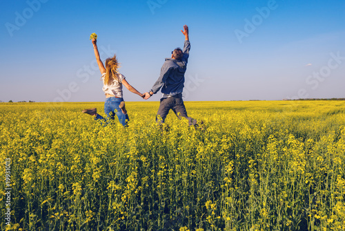 Obraz na płótnie Joyful couple with open arms is jumping on the field w salonie