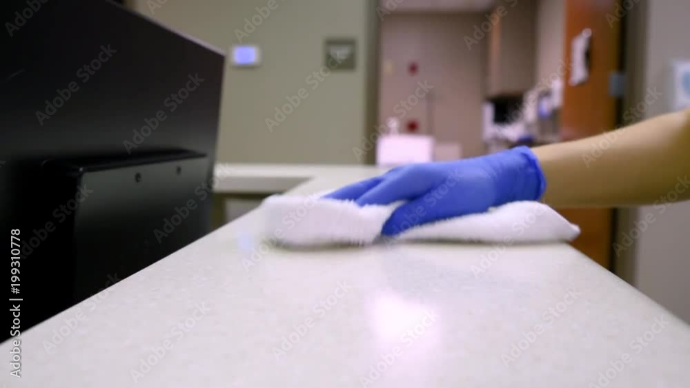 Janitor cleaning medical office counter top using sanitizing antibacterial spray in hospital doing custodian work alone at night