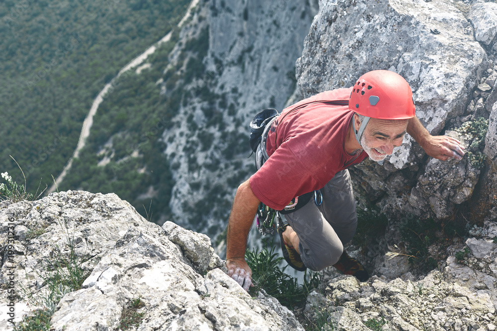old-aged man rock climber climbs on the cliff