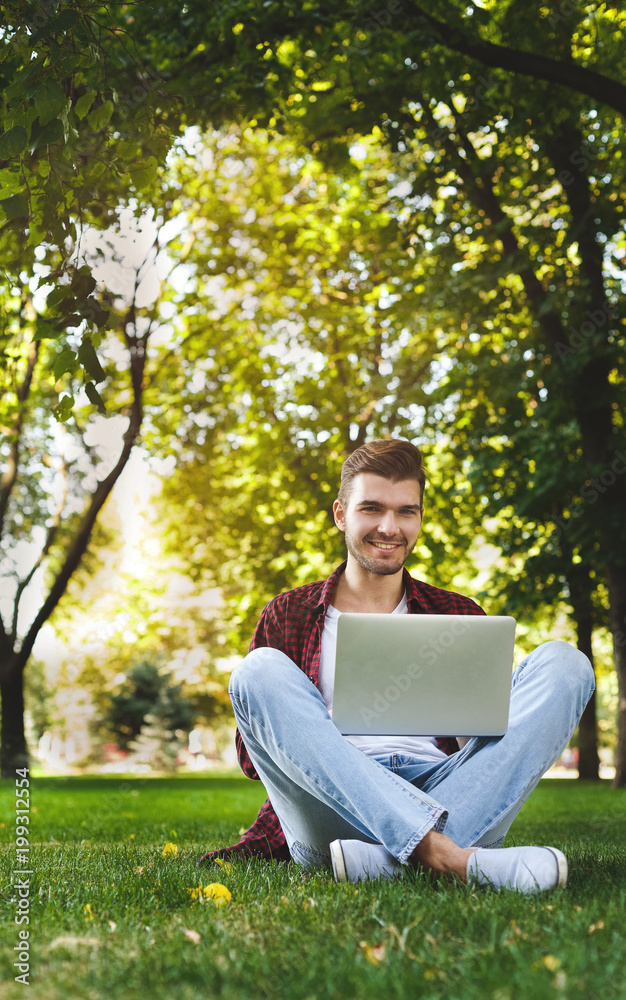 Obraz premium Happy man is sitting in the park and using laptop
