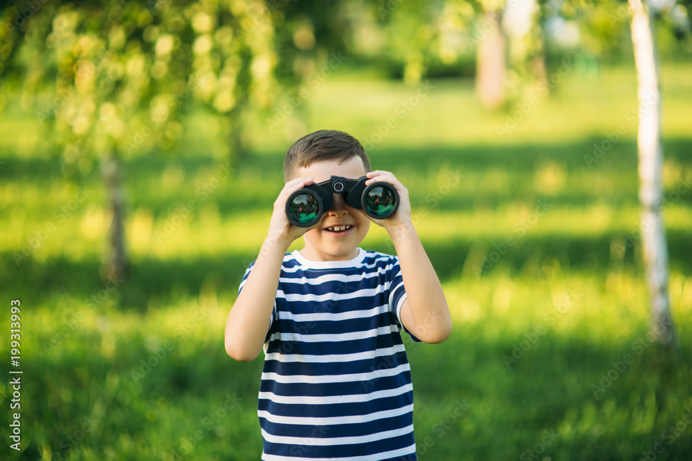 Little boy in a striped t-shirt looks through binoculars .Spring, sunny weather Little boy in a striped t-shirt looks through binoculars .Spring, sunny weather