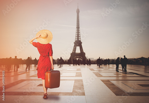 Redhead girl with suitcase in Paris with Eiffel tower on background. Concept of travelling around the World © Masson