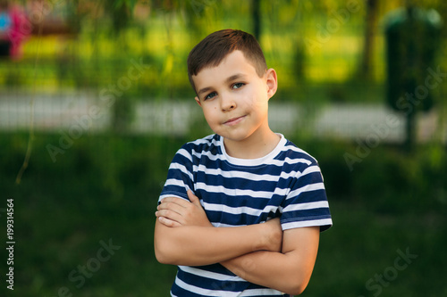 A little boy in a striped T-shirt standing in front of green background. Smiling and looking to the photographer.