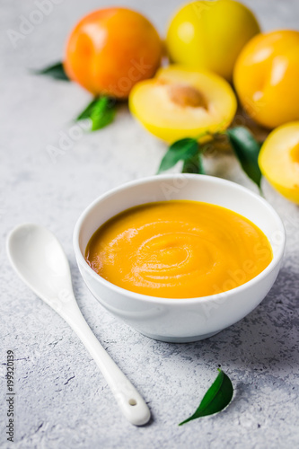 Baby food, yellow plum sauce in ceramic bowl and fresh golden plums on concrete background. Selective focus, space for text. 