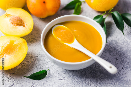 Sweet and spicy yellow plum sauce in ceramic bowl and fresh golden plums on concrete background. Selective focus, space for text. 