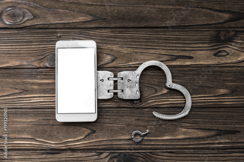 Wallpaper Mural smartphone with white screen, handcuffs on a wooden background. dependence on the Internet, mobile communications. Torontodigital.ca