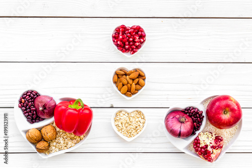 Diet for healthy heart. Food with antioxidants. Vegetables, fruits, nuts in heart shaped bowl on white wooden background top view copy space