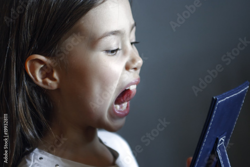 The girl in front of the mirror does logopedic exercises. Gymnastics for the tongue
