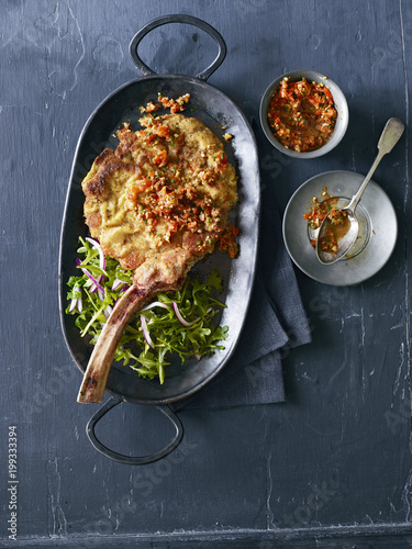 Fried veal chop and arugula with tomato garnish