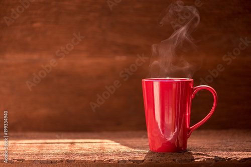 red coffee cup with smoke stream on wooden table under moring sunlight