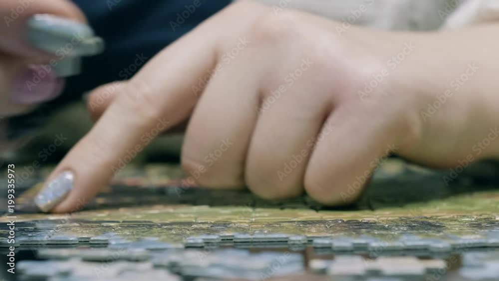 Close up of a young woman's fingers as she tries to find where a puzzle piece fits in a large puzzle Close up of a young woman's fingers as she tries to find where a puzzle piece fits in a large puzzle
