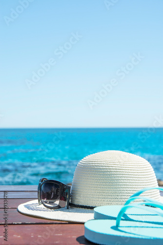 Hat Sunglasses Slippers on Blue Sky and Turquoise Sea Background. Summer Vacation Travel Relaxation. Idyllic Seascape View. Beautiful Scenery. Copy Space