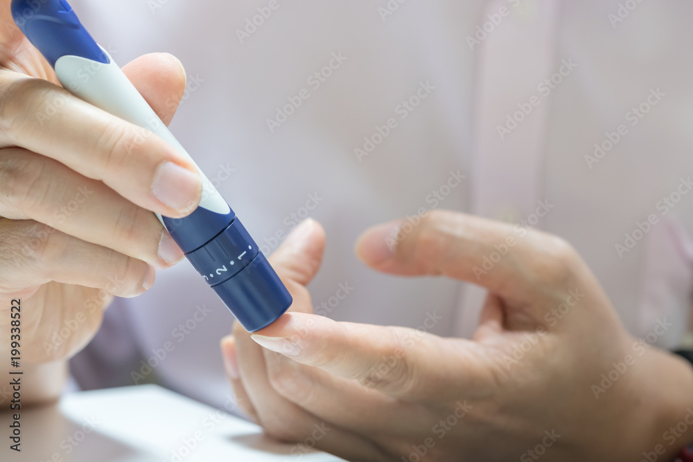 Close up of man hands using lancet on finger to check blood sugar level by Glucose meter using as Medicine, diabetes, glycemia, health care and people concept.