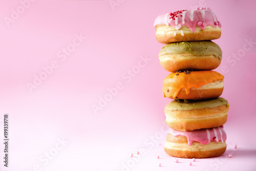 Stack of glazed colorful assorted donuts with sprinkles on pink background. Copy space. Sweet doughnuts for kids