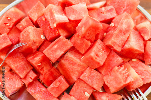 Metal oval dish with a bunch of slices of sliced juicy watermelon with dessert forks on wooden background in sunlight, close up