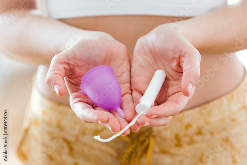 Young woman hands holding different types of feminine hygiene products - menstrual cup and tampons. photo