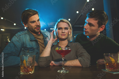 I do not want to tell about it. Portrait of disappointed female talking with two interested guys. Acquaintance with men in club concept