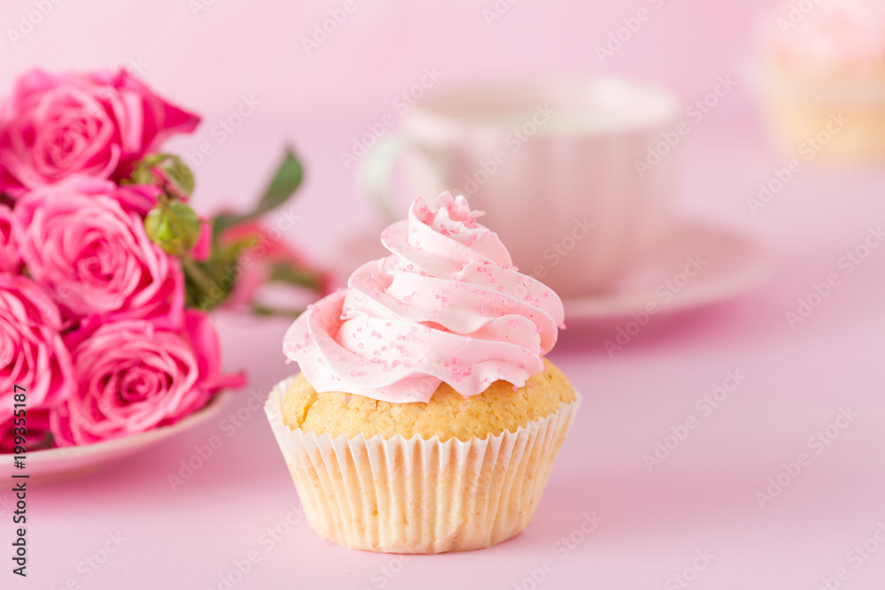 Cupcake with pink cream decoration and roses on pink pastel background.