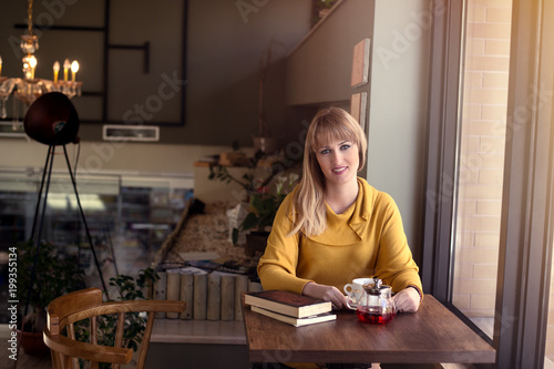 attractive blond woman in a cafe drinking tea and readig a book early morning