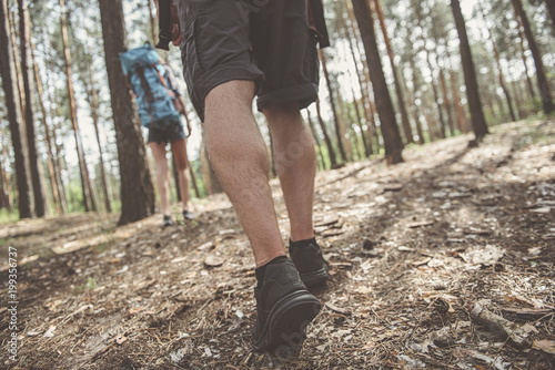 Active lifestyle. Low angle close up of feet of young energetic tourist who is going across forest. Girl with backpack is traveling on background