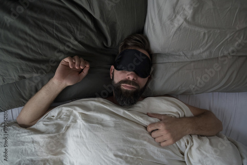 High angle view of man wearing sleep mask while sleeping on bed at home